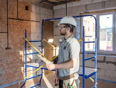 Bir elektrikçi, inşaat alanındaki çizimleri inceler..