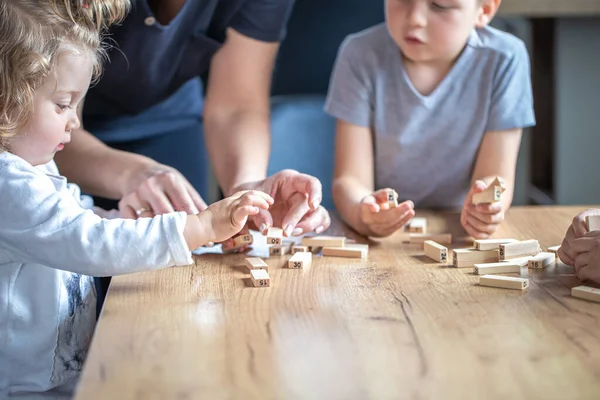 Small children play board game with wooden cubes at home in the kitchen with mom.