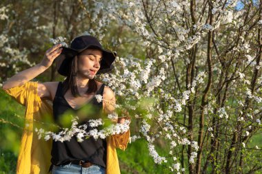 Çiçek açan ağaçların arasında şapkalı çekici bir kız bahar çiçeklerinin kokusundan hoşlanır..