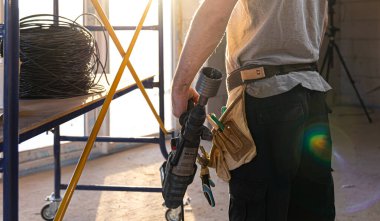 Bir tamirci güneşli bir odada elinde bir sondaj aleti tutar..