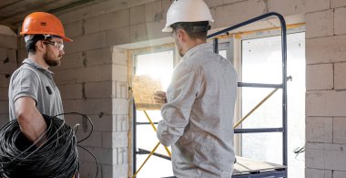 İnşaat alanında konuşan iki mühendis, bir işçiye çizimi açıklayan mühendis..