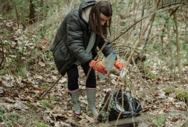 Çöp torbasıyla gönüllü bir kız ormandaki çöpleri temizliyor..