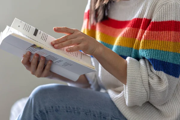Close-up of an open book in the hands of a girl in a bright colored sweater.