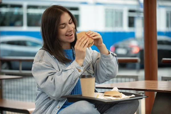 평상복 차림의 매력적 소녀가 여름철 테라스에 커피와 햄버거를 먹는다 — 스톡 사진