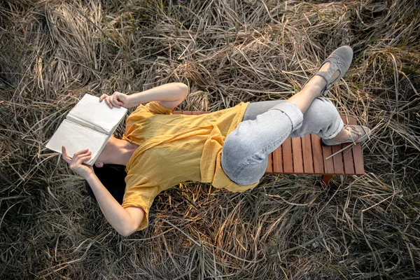 Bir Kız Çimler Arasında Kitap Okuyor Bankın Üstünde Yatıyor — Stok fotoğraf