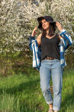 Baharda çiçek açan ağaçların arasında şapkalı neşeli bir kız, sıradan bir tarzda..