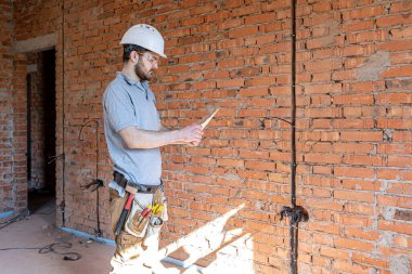 İş kıyafetli bir müteahhit inşaat alanındaki bir çizimi inceliyor..