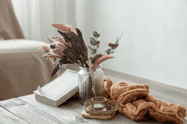 Odanın içinde bir kitap, kuru bir çiçek ve örgü ögesi olan bir kompozisyon..