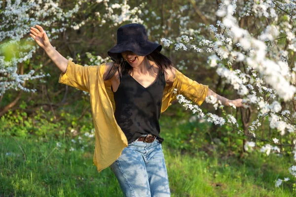 春の花の香りを楽しむ花の木の間の帽子の魅力的な女の子 — ストック写真