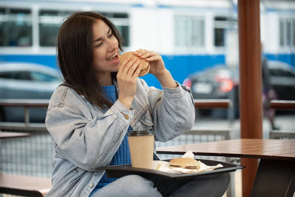 평상복 차림의 매력적 소녀가 여름철 테라스에 커피와 햄버거를 먹는다 — 스톡 사진