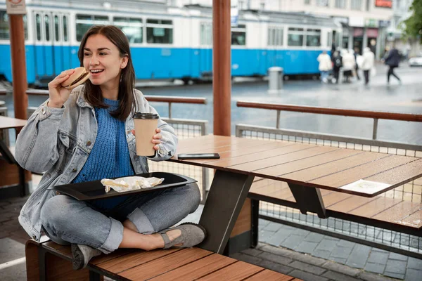평상복 차림의 매력적 카페의 여름철 테라스에 커피를 마시며 햄버거를 먹는다 — 스톡 사진