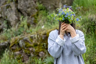 Kız yüzünü ormanda toplanan bir buket taze çiçeğin arkasına saklar..