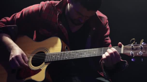 男性ギタリストが暗室でアコースティックギターのコードを演奏する — ストック動画