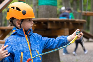 Yüksek telli parka tırmanma macerası. Küçük çocuk dağ kaskı ve güvenlik ekipmanlarıyla rotasında ilerliyor..