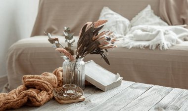 Odanın içinde bir kitap, kuru bir çiçek ve örgü ögesi olan bir kompozisyon..