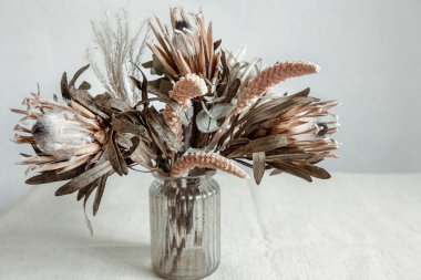 Bir buket kurumuş çiçek, arka planda cam bir vazoda..