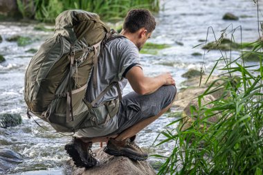 Yaz sıcağında dağ nehrinin yanında büyük bir sırt çantasıyla gezen bir turist..
