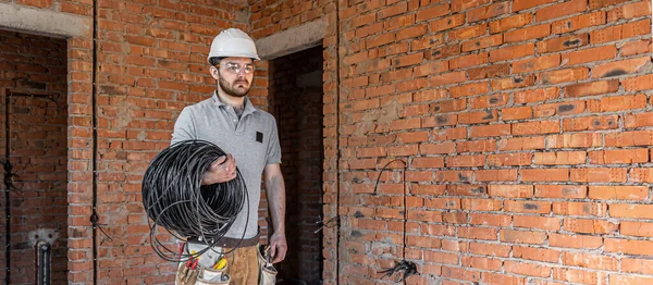 Electricista Con Sombrero Duro Mira Pared Mientras Sostiene Cable Eléctrico —  Fotos de Stock