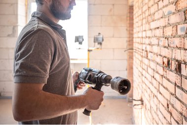 Duvarı delmek için delme işlemi sırasında inşaat alanında çalışan bir tamirci..