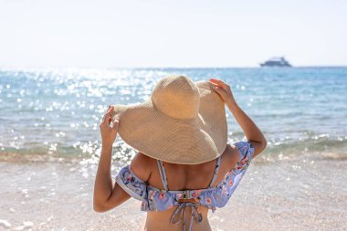 Büyük şapkalı bir kadın deniz kenarında güneşleniyor..
