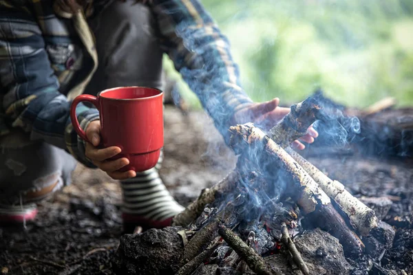 A cup with a warm drink while hiking in the woods by the fire.