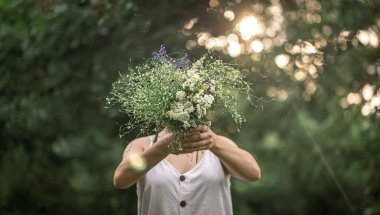 Ormandaki bulanık arka planda bir kızın elinde bir buket yabani çiçek..