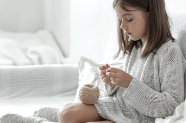 Evinde kanepede iplik yumağı ve iğne taşıyan küçük bir kız..