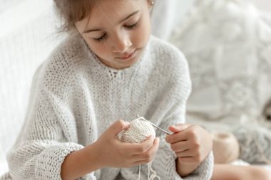 İplikleri olan küçük bir kız örgü örmeyi, ev işlerini ve dikiş işlerini öğreniyor..