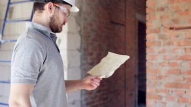 İnşaatçı, ustabaşı inşaat alanında durur ve binanın projesine bakar..