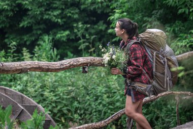 Seyahat için büyük bir sırt çantası ve bir buket kır çiçeğiyle çekici bir kız turist..