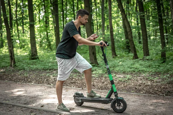 Sokakta Elektrikli Scooterla Dikilirken Akıllı Telefonunu Kullanan Genç Çekici Bir — Stok fotoğraf