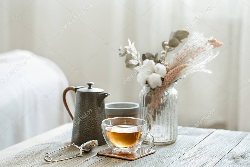 Cozy still life with glass cup of tea, candles and knitted element on blurred background copy space.