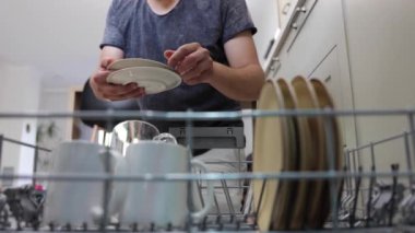 Bir adam bulaşık makinesine kirli bulaşıkları ve diğer bulaşıkları koyar..