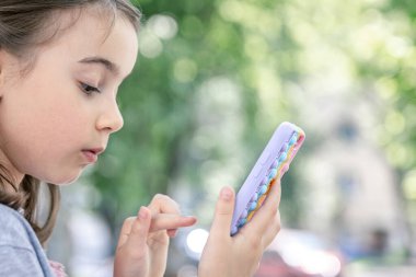 Küçük bir kız elinde sivilceli bir çantada bir telefon tutuyor onu patlatıyor, son moda stres önleyici oyuncak..