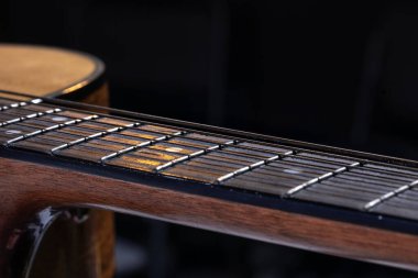 Akustik gitarın bir parçası, siyah arkaplandaki dizgileri vurgulayan gitar fretboard 'u.