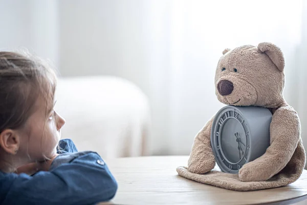 Kleines Mädchen Blickt Traurig Auf Einen Teddybär Mit Wecker Auf — Stockfoto