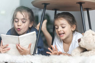İki küçük kız kardeş yerde uzanmış bir kitap okuyorlar..