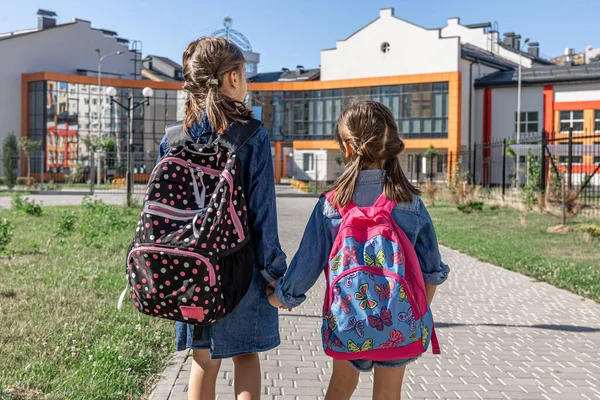 Pupils of primary school. Girls with backpacks near school outdoors. Beginning of lessons. Back yo school.