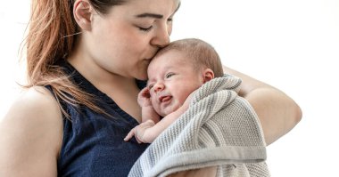 Genç bir anne, beyaz bir arka planda yeni doğmuş oğlunu kollarına alıp öpüyor..
