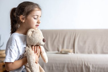 Üzgün küçük kız ve oyuncak ayı bulanık arka plan fotokopi uzayında evde..