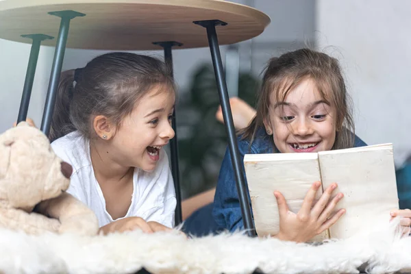 Две Младшие Сестры Читают Книгу Лежащую Полу Уютном Одеяле — стоковое фото
