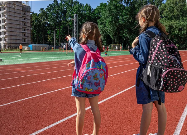 小女孩背着背包在体育馆上学 看着男孩子踢足球 — 图库照片