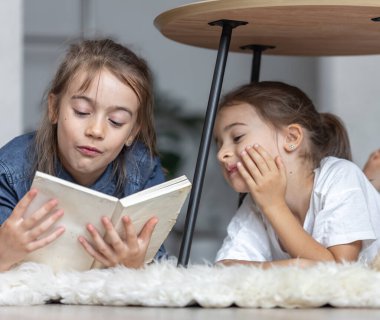 İki küçük kız kardeş odalarında yerde yatarken birlikte kitap okurken eğleniyorlar..