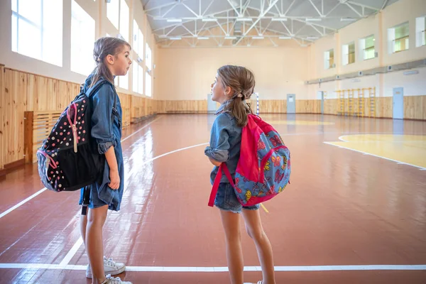 Małe Słodkie Dziewczynki Uczennice Plecakami Szkole Pustej Sali Gimnastycznej Szkoły — Zdjęcie stockowe