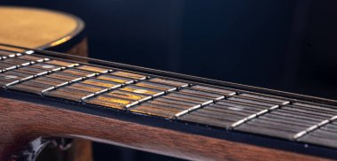 Akustik gitarın bir parçası, siyah arkaplandaki dizgileri vurgulayan gitar fretboard 'u.