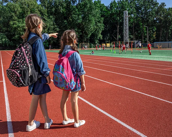 小さな女の子の学校の子供たちはスタジアムでバックパックを着て少年たちがサッカーを見て — ストック写真