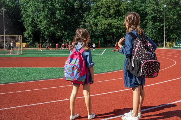 小さな女の子の学校の子供たちはスタジアムでバックパックを着て少年たちがサッカーを見て — ストック写真