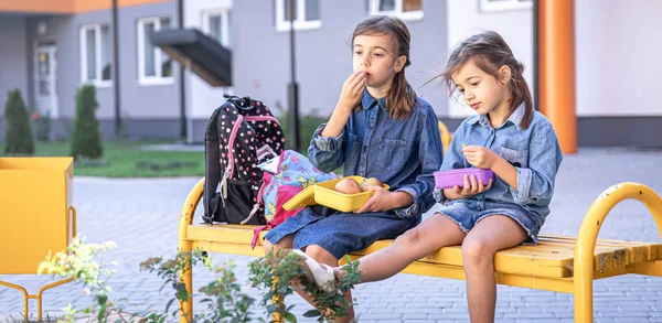 学校に戻る 可愛いです小さな女の子は学校の庭にベンチに座って昼食を屋外で食べる — ストック写真