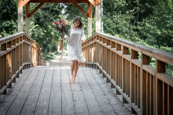 美丽的姑娘 身穿白色的连衣裙 木桥上有一束奇异的花朵 — 图库照片