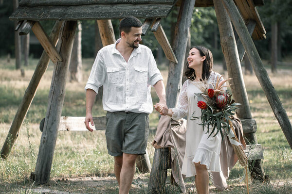 Young man and woman smartly dressed, with a bouquet of exotic flowers are walking in the woods, on a date in nature.